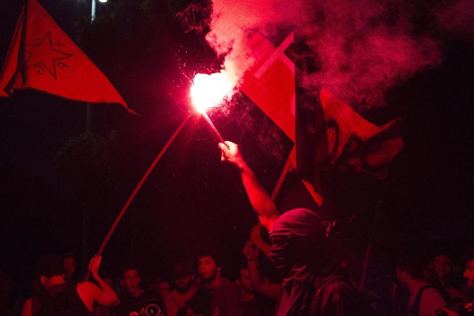 A masked demonstrator holds up a flare during a demonstration against government proposed changes to work rules and pensions in Rio de Janeiro, Brazil, Wednesday, March 15, 2017. Critics say the changes would reduce job security for Brazilian workers and the pension proposal would force many people to work longer to qualify for pensions and reduce retirement benefits for many. (AP Photo/Leo Correa)