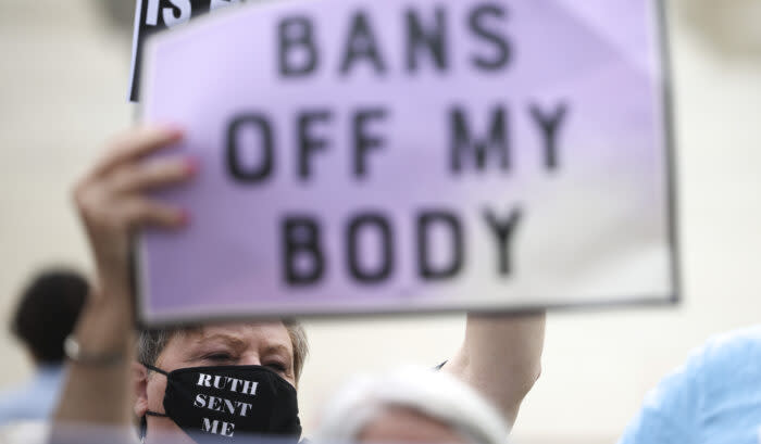 A woman wearing a mask and holding a sign saying "Bans Off My Body"