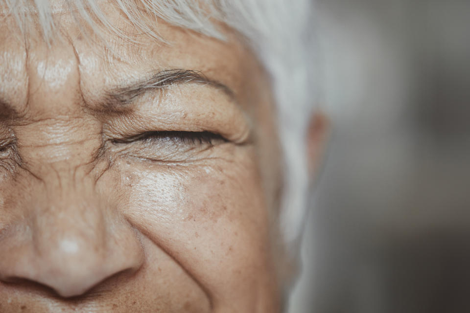 Close-up of an elderly person's face with eyes tightly shut, highlighting wrinkles and skin texture