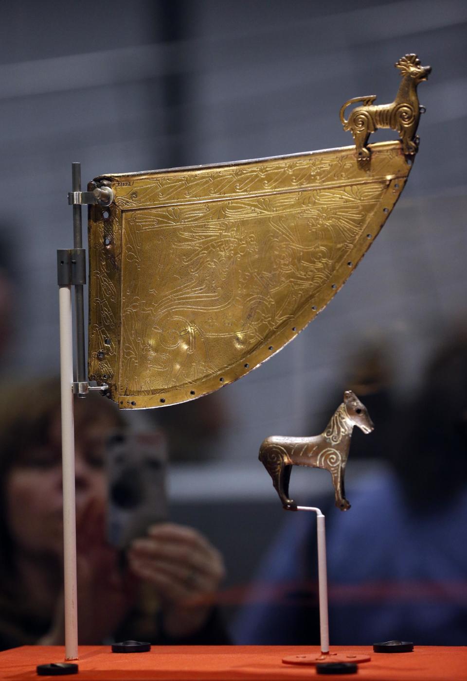 A visitor takes pictures of a Viking horse statuette and a decorated warship weathervane at a new exhibition entitled 'Vikings: Life and Legend' at the British Museum in central London, Tuesday, March 4, 2014. The new exhibition strives to make people think again about the Scandinavian pillagers who raided and struck terror into English villages. The exhibition aims to show how Viking energy and ideas re-drew the map of the world, through the presentation of their ships, their weapons, their crafts, their words and even their skeletons. (AP Photo/Lefteris Pitarakis)