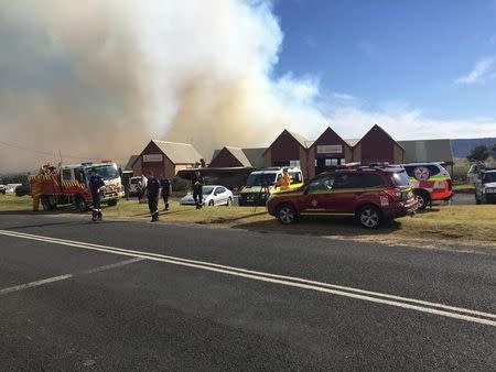 Firefighters stand near their vehicles as smoke rises in the background from a bushfire in New South Wales, Australia, August 16, 2018, in this picture obtained from social media. Fire and Rescue NSW/via REUTERS