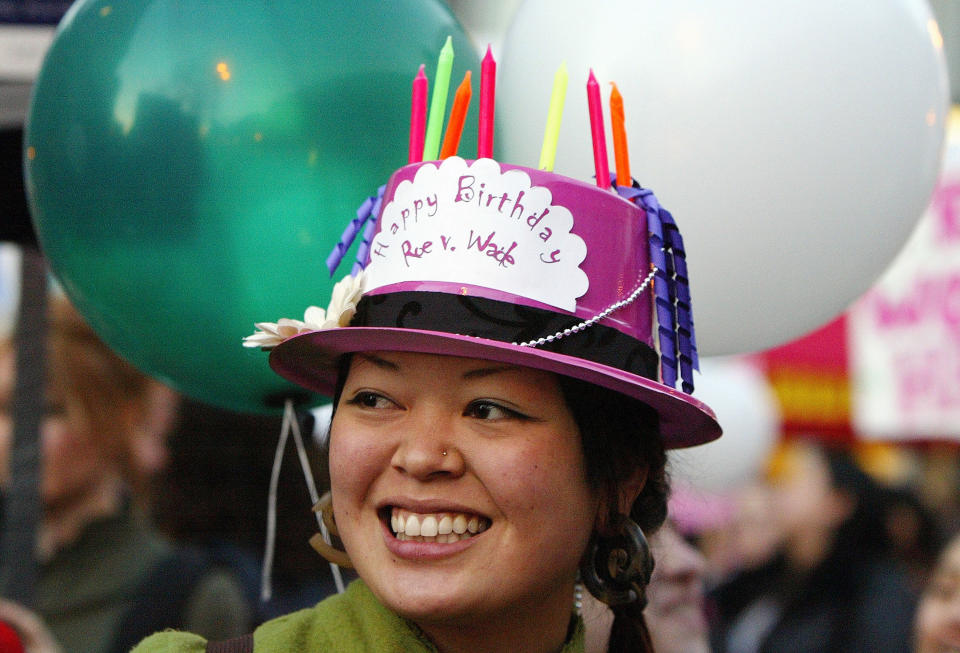 A person wears a hat with birthday candles and a small paper decoration reading "happy birthday roe v wade"