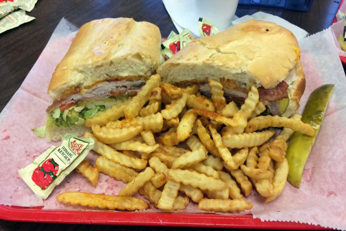 Mike's Deluxe Sandwich with lots of fries in front of it on serving paper on a red tray, United Deli and Grocery, Columbus, Mississippi, on a wooden veneer table