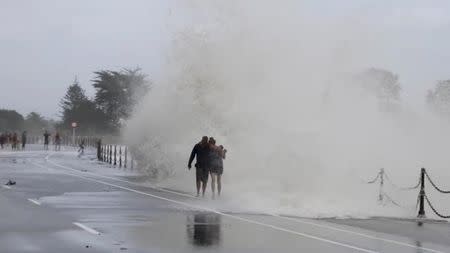 A wave crashes on the shore as people walk along a road in Nelson, after former Tropical Cyclone Fehi descended upon New Zealand, in this still image taken from a February 1, 2018 social media video. Leroy Bull Photography/via REUTERS