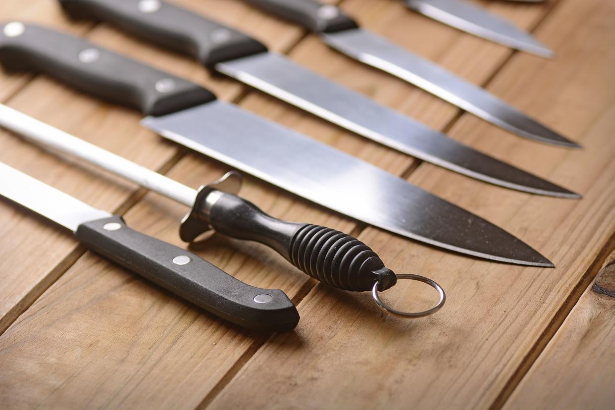 Five knives with a knife sharpener, in a set, on a wooden table, blurred towards the top right