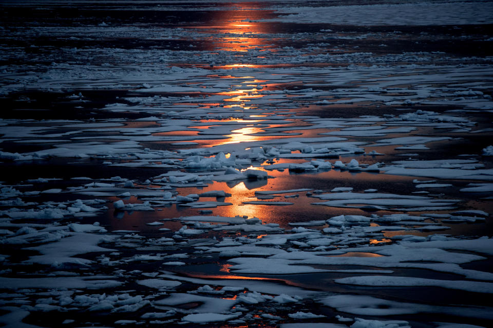 FILE - The midnight sun shines across sea ice along the Northwest Passage in the Canadian Arctic Archipelago, Sunday, July 23, 2017. When covered with snow and ice, the Arctic reflects sunlight and heat. But that blanket is dwindling. And as more sea ice melts in the summer, “you’re revealing really dark ocean surfaces, just like a black T-shirt,” says ice scientist Twila Moon. Like dark clothing, the open patches of sea soak up heat from the sun more readily. (AP Photo/David Goldman, File)