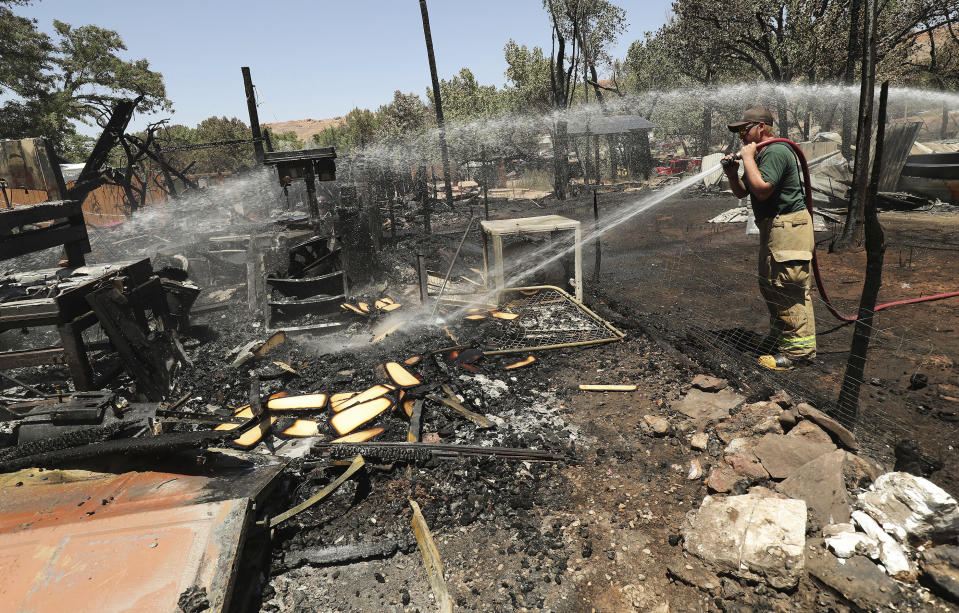 <p>A Green River firefighter cleans up after a brush fire near Pack Creek in Moab, Utah, Wednesday, June 13, 2018. A fast-moving brush fire destroyed homes in the Utah tourist town of Moab, while several thousand people in Colorado and Wyoming fled multiple wildfires scorching the drought-stricken U.S. West on Wednesday. (Photo: Jeffrey D. Allred/The Deseret News via AP) </p>