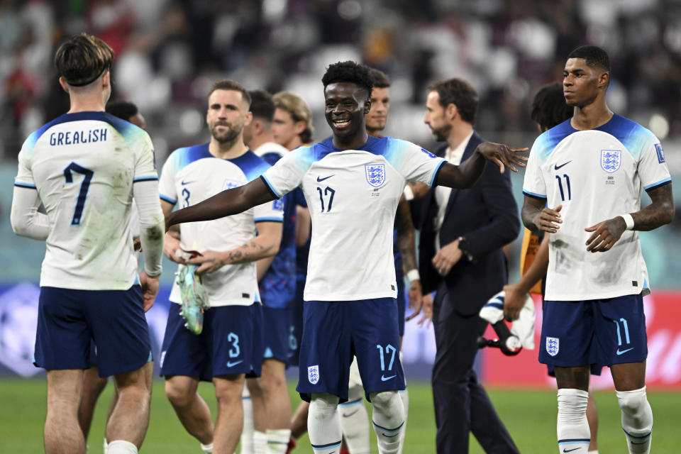 England's Bukayo Saka cheers after the final whistle, having scored two of the Three Lions' six goals against Iran. Coach Gareth Southgate walks in the background, at Qatar's Chalifa International Stadium, Nov. 21, 2022.<span class="copyright">Robert Michael—picture-alliance/dpa/AP</span>