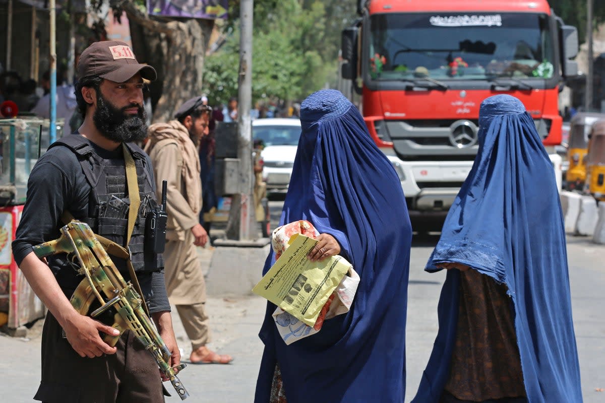 Afghan burqa-clad women walk past a Taliban security personnel along a street in Jalalabad (AFP via Getty Images)