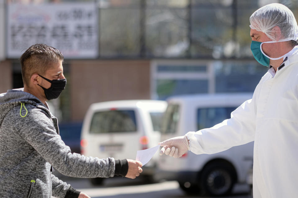 A man wearing a protective face mask hands a paper to a member of the medical staff at the Vrazova community health center in Sarajevo, Bosnia, Tuesday, April 7, 2020. Less than three weeks ago, the respected Bosnian epidemiologist Sefik Pasagic was fielding calls from journalists seeking his opinion and advice on how best to prepare for the coronavirus outbreak. The 60-year-old father of four died of complications from the COVID-19 infection which his wife describes as an unnecessarily long and desperate struggle to get the help he needed.(AP Photo/Kemal Softic)