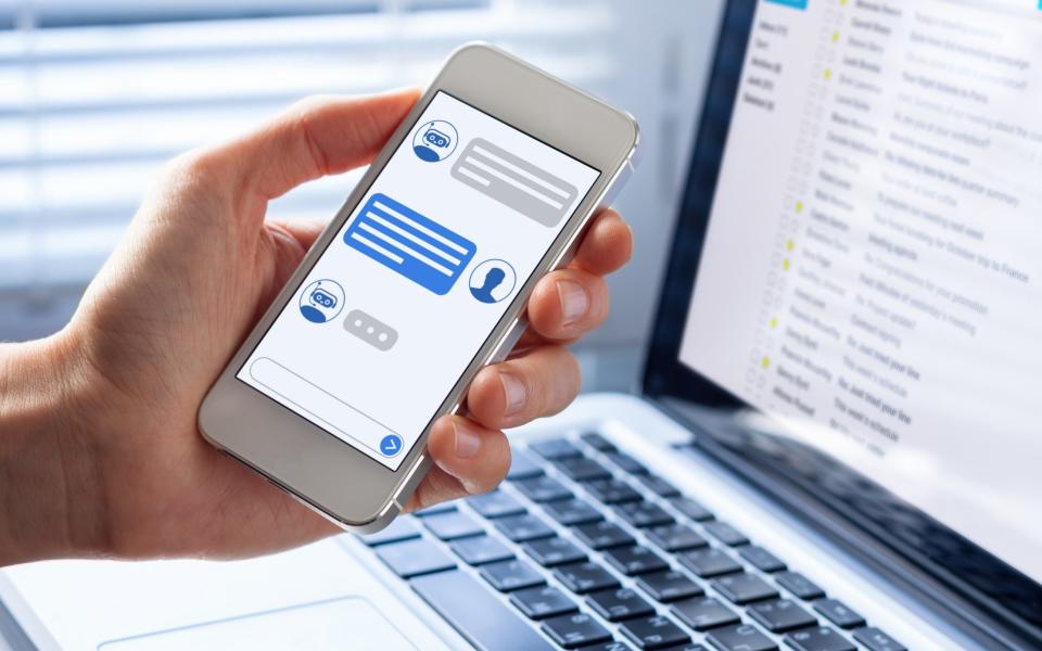 Chatbot conversation on smartphone screen app interface with artificial intelligence technology providing virtual assistant customer support and information, person hand holding mobile phone - NicoElNino/iStockphoto