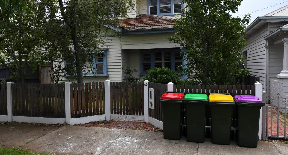 Four coloured bins outside home with fence. 