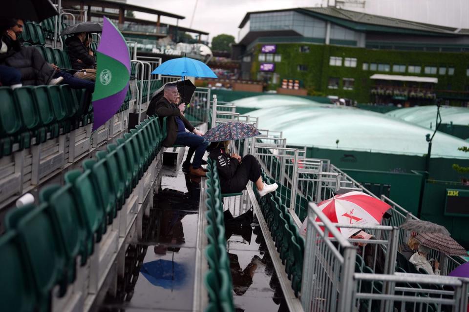 Spectators shelter beneath umbrellas as rain stops play on uncovered courts at Wimbledon on Tuesday (Jordan Pettitt/PA Wire)