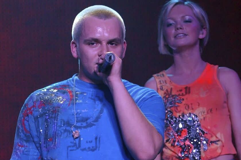 Pop singer Paul Cattermole sings into a microphone while his bandmate stands behind him