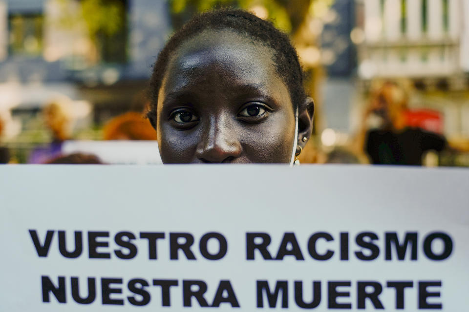 A woman holds up a banner that reads: "Your Racism, Our Dead", during one of many protests across Spain amid for the investigation over the deaths of at least 23 people at the border between the Spanish enclave of Melilla and Morocco, in Pamplona, northern Spain, Friday, July 1, 2022. (AP Photo/Alvaro Barrientos)