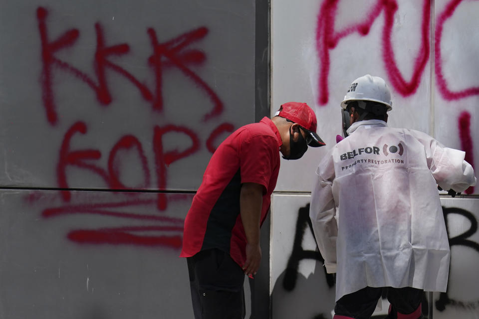 Workers prepare to clean graffiti off the outside of the an Oakland Police Department building in Oakland, Calif., Sunday, July 26, 2020. A protest through the streets of downtown Oakland, California, in support of racial justice and police reform turned violent when "agitators" among the demonstrators set fire to a courthouse, vandalized a police station and shot fireworks at officers, authorities said. (AP Photo/Jeff Chiu)