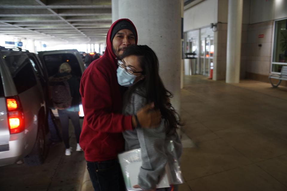 A man embraces a woman in a mask at the airport.