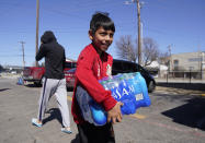 FILE - In this Feb. 23, 2021, file photo, Diego Garcia, 9, carries drinking water he was given by volunteers at an apartment complex without water in Dallas. Two local bartenders took it upon themselves to bring a truck of drinking water to distribute to residents that have not had running water for over a week. (AP Photo/LM Otero, File)