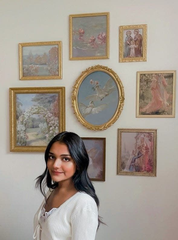 Gloria John, 21, stands in front of framed wall hangings she made entirely from thrifted items and DIY prints.