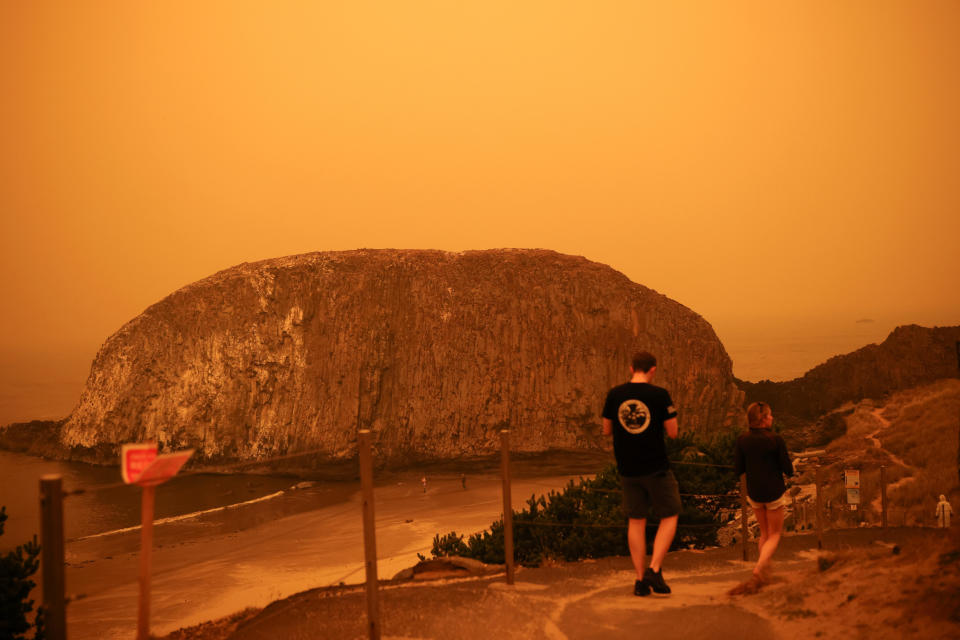 People walk by the Pacific Ocean coast as smoke from wildfires covers an area near Seal Rock, Oregon, on September 8, 2020. / Credit: CARLOS BARRIA / REUTERS