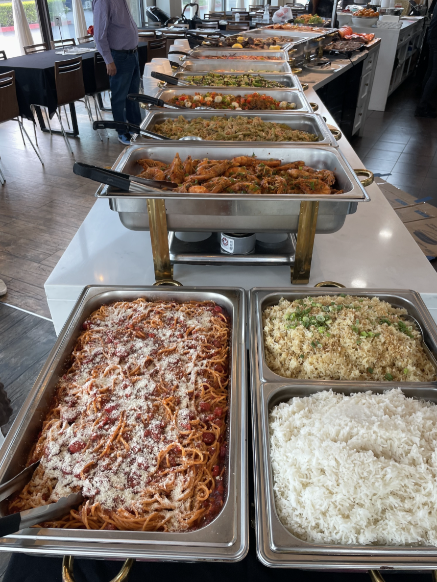 Close-up of a buffet table filled with various dishes including pasta, rice, vegetables, and other entrees in stainless steel serving trays