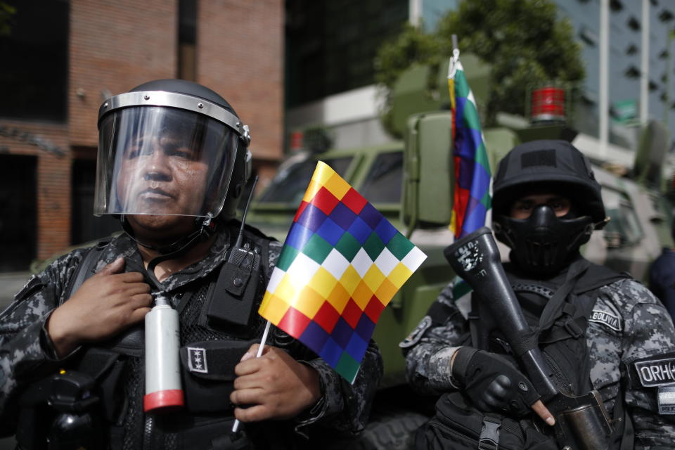 A police officer holds a "wiphala" flag, representing indigenous people, that he was given by supporters of former President Evo Morales who are marching in La Paz, Bolivia, Tuesday, Nov. 12, 2019. Former President Evo Morales, who transformed Bolivia as its first indigenous president, flew to exile in Mexico on Tuesday after weeks of violent protests, leaving behind a confused power vacuum in the Andean nation. (AP Photo/Natacha Pisarenko)