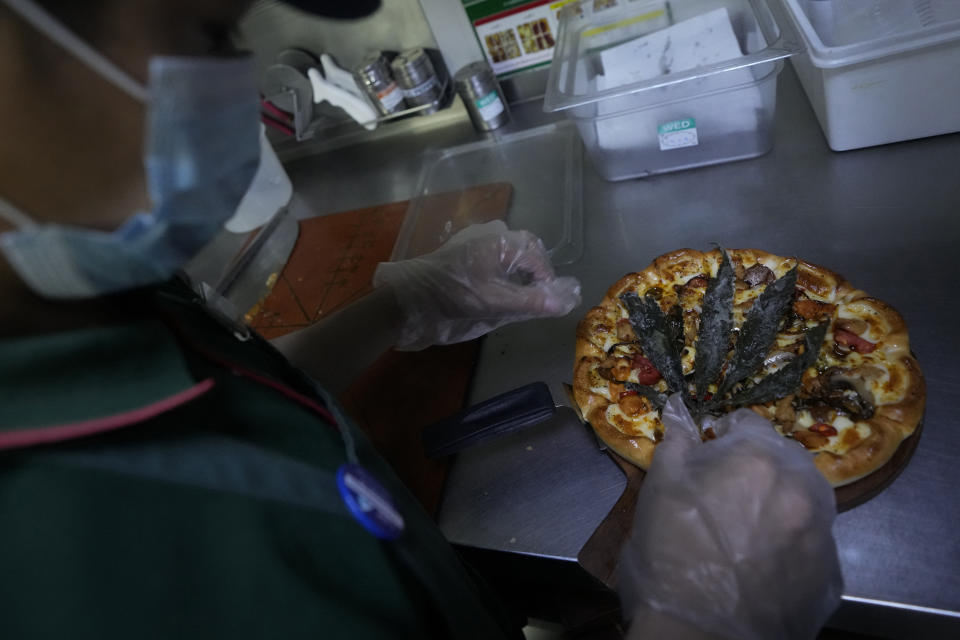 A staff member prepares a pizza with a deep fried cannabis leaf at a restaurant in Bangkok, Thailand on Nov. 24, 2021. The Pizza Company, a Thai major fast food chain, has been promoting its "Crazy Happy Pizza" this month, an under-the-radar product topped with a cannabis leaf. It’s legal but won’t get you high. (AP Photo/Sakchai Lalit)