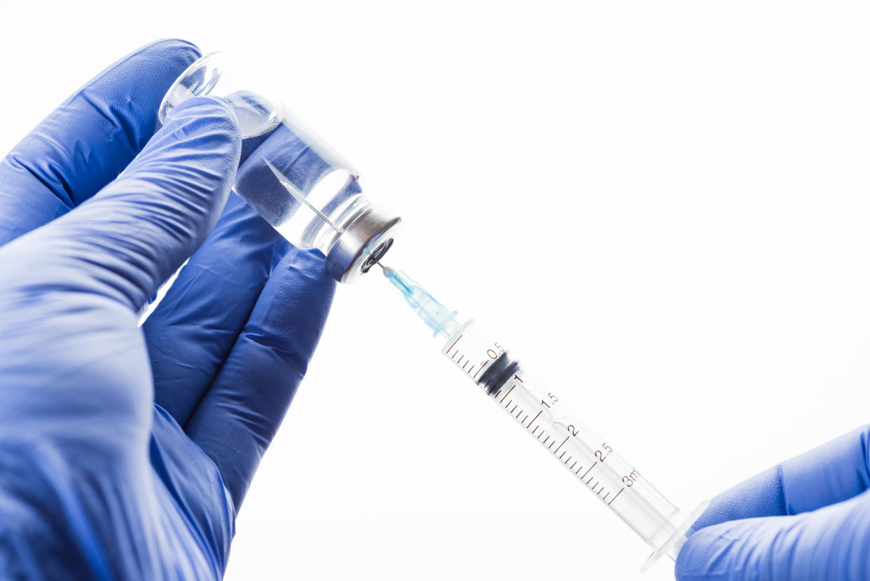 The doctor fills a syringe. Glass bottle with a transparent antibiotic or vaccine in the hands in blue latex gloves.