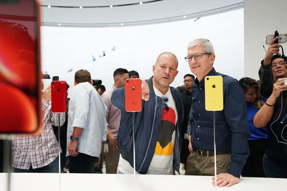 Tim Cook and Jony Ive look at the iPhone XR with a crowd of people in the background.
