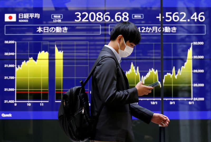 A man walks past an electric monitor displaying Japan's Nikkei share average and recent movements, outside a bank in Tokyo