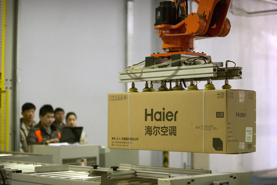 In this Friday, Feb. 24, 2017 photo, factory workers watch as a machine uses suction to lift a box containing an air conditioner at a Haier factory in Jiaozhou near Qingdao in eastern China's Shandong Province. Zhang Ruimin built Haier from a failing refrigerator factory in the 1980s into the biggest maker of major appliances. Now, he is trying to transform a traditional manufacturer with 60,000 employees in 25 countries into a nimble, Internet Age seller of consumer goods and services from web-linked washing machines to food delivery. (AP Photo/Mark Schiefelbein)