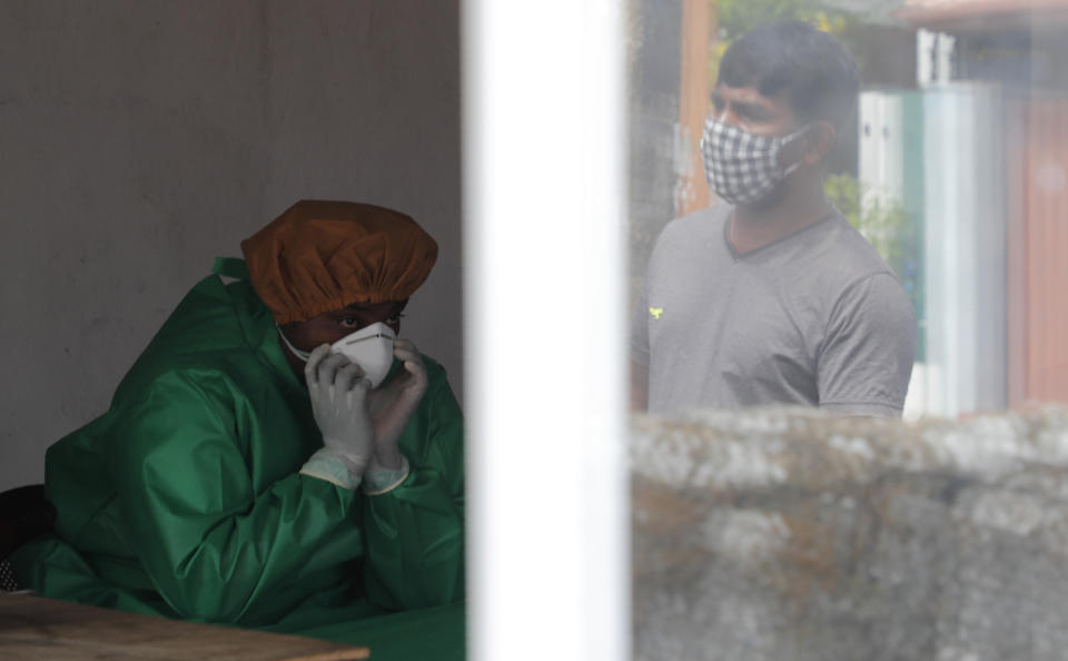 A Sri Lankan municipal health worker takes a breather while collecting swab samples to test for COVID-19, as a man waiting for his turn to test is seen reflected on a window in Colombo, Sri Lanka, Friday, July 10, 2020. (AP Photo/Eranga Jayawardena)