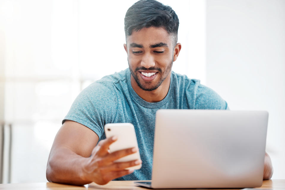 Attractive man using smartphone with laptop nearby. 