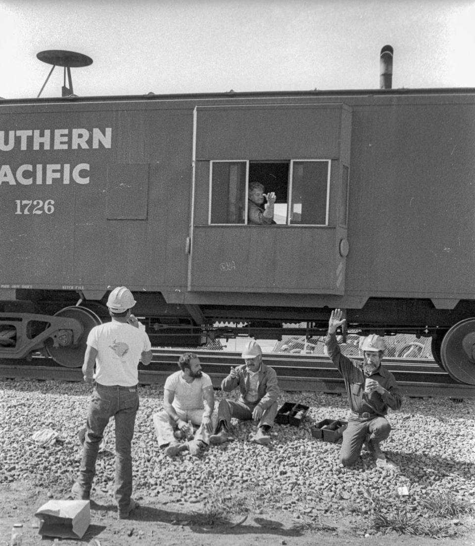 Workers on a lunch break wave to a passing Southern Pacific caboose in San Luis Obispo on March 12, 1984.