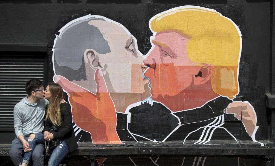 In this 2016 photo, a couple kisses in front of graffiti depicting Russian President Vladimir Putin and Donald Trump kissing in Vilnius, Lithuania. (AP Photo/Mindaugas Kulbis)