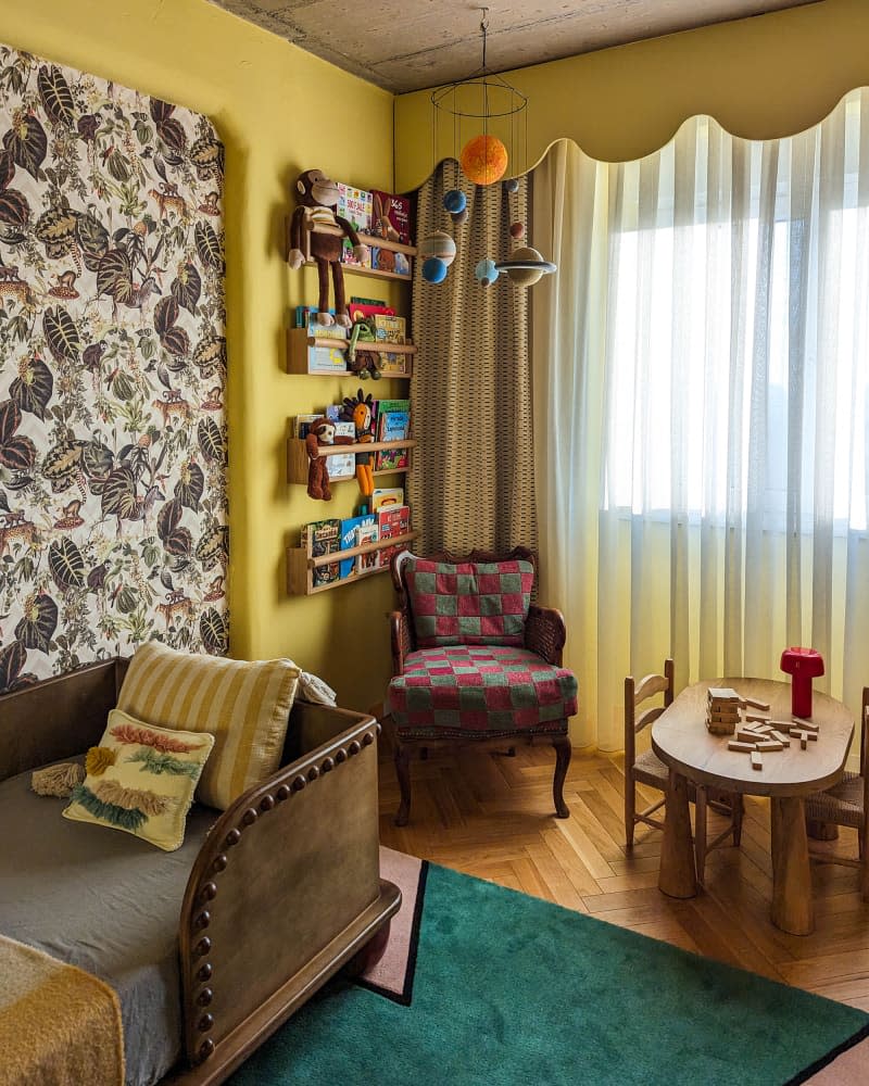 Yellow kids room with botanical wallpaper accent wall, brown leather and wood bed, vintage armchair, and activity table