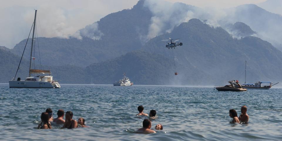 People in the water looking at a hill with smoke rising