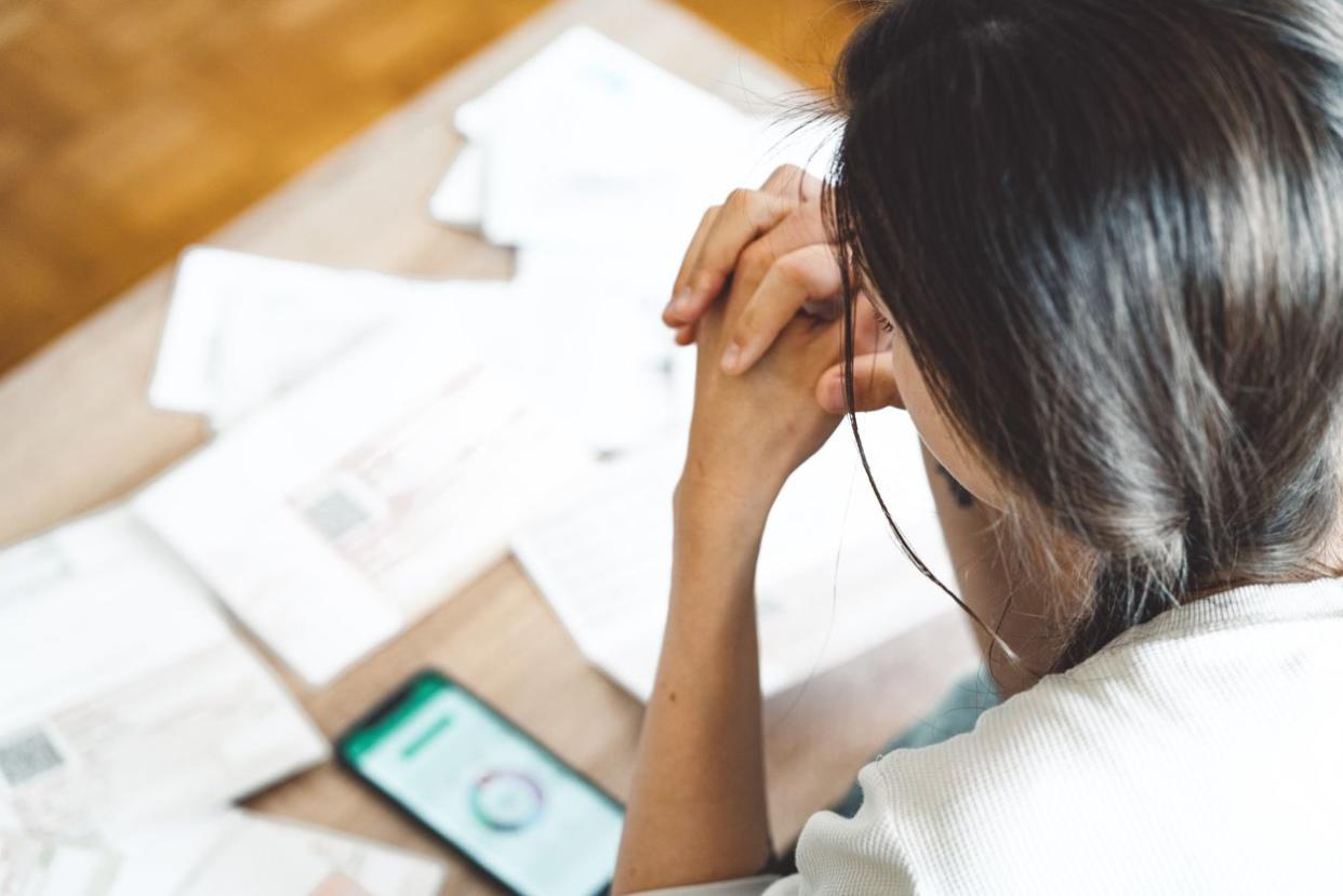 backside of concerned woman on right side looking down on table of bills and smartphone on left side