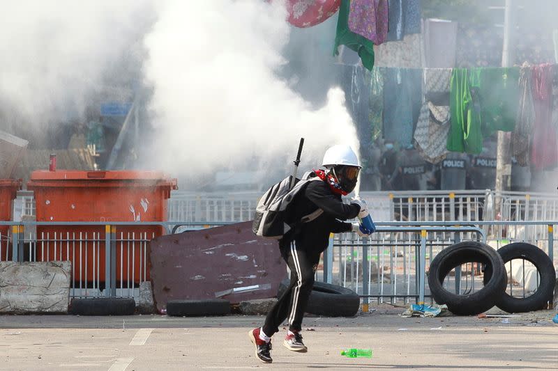 An anti-coup demonstrator sprays a fire extinguisher as he runs away from a barricade during a protests in Yangon