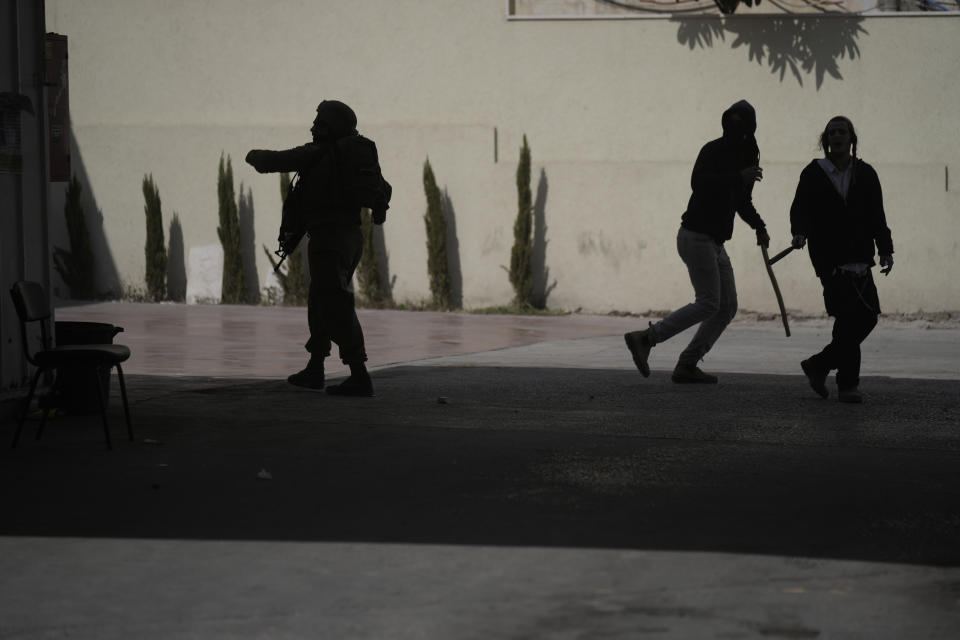 An Israeli soldier, left, and Israeli settlers with sticks, during clashes when settlers attacked Palestinians in Huwara, near the West Bank town of Nablus, Thursday, Oct. 13, 2022. (AP Photo/ Majdi Mohammed)