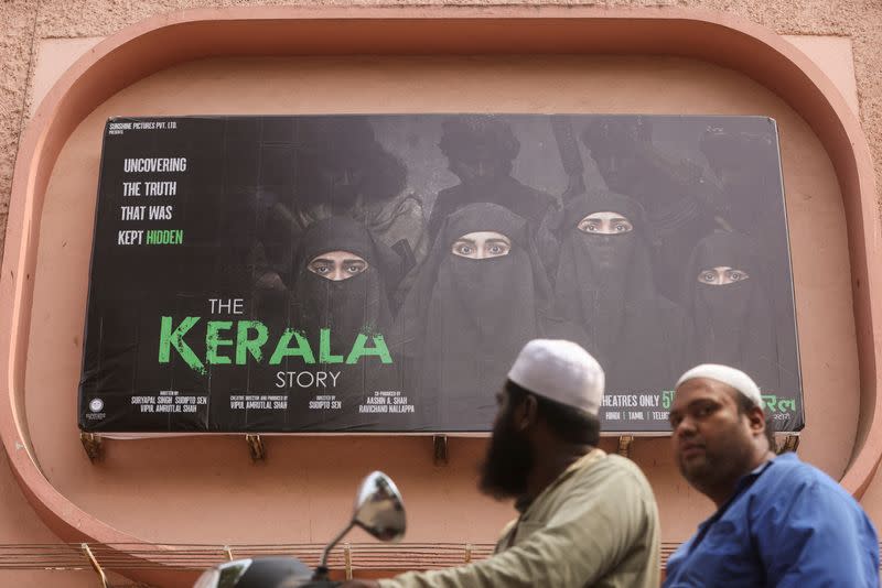 FILE PHOTO: People ride past a poster of a Hindi movie titled "The Kerala Story", outside a cinema in Mumbai