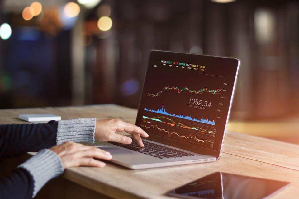 Person looking at stock information on a laptop at a wooden desk.