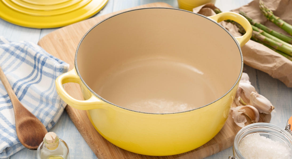  An empty yellow Dutch oven with the lid removed sitting on a chopping board surrounded by ingredientsh. 