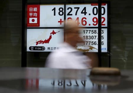 A pedestrian walks past electronic boards showing the Japan's Nikkei average outside a brokerage in Tokyo, Japan, September 9, 2015. REUTERS/Yuya Shino