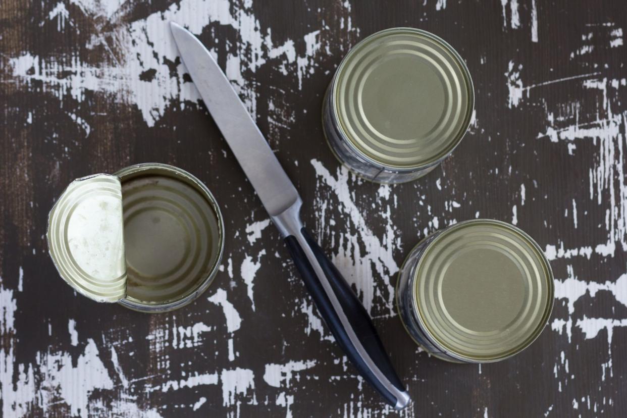 Top view of two closed cans and one open can with knife on wooden background