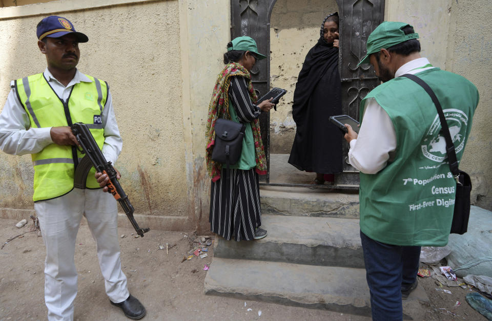 A police officer, left, stands guard as a government workers collect data from a woman during census, in Peshawar, Pakistan, Wednesday, March 1, 2023. Pakistan on Wednesday launched its first-ever digital population and housing census to gather demographic data on every individual ahead of the parliamentary elections which are due later this year, officials said. (AP Photo/Fareed Khan)