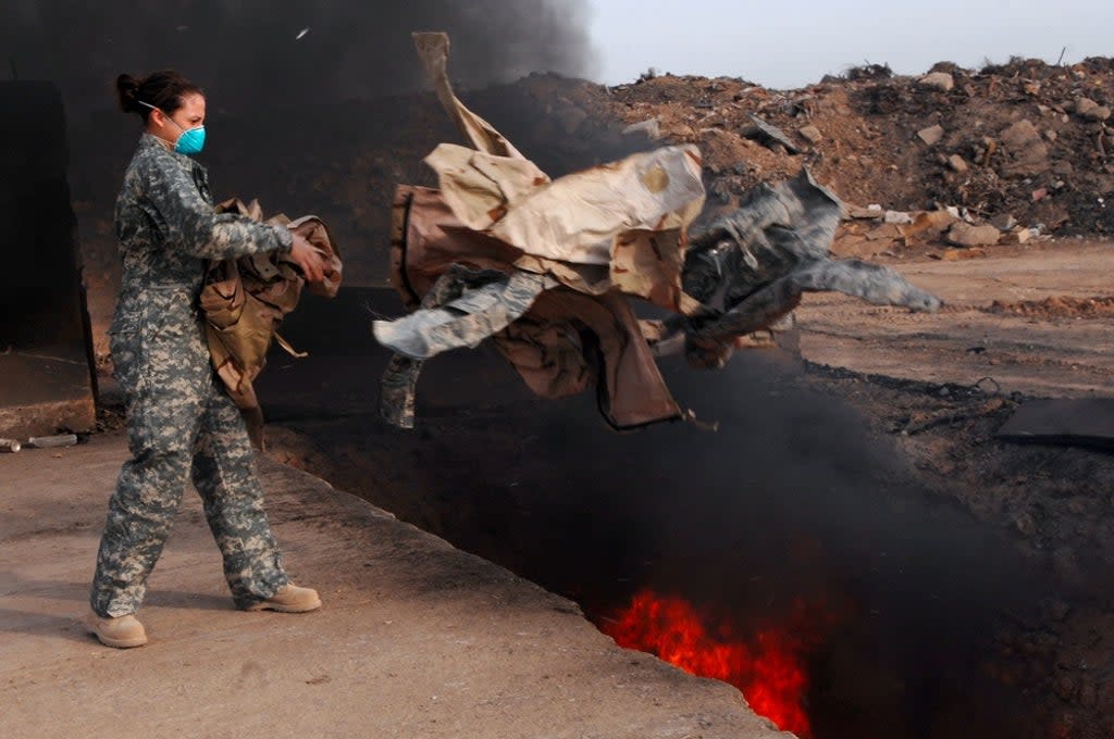 A US servicemember tosses trash into a huge burn pit  (U.S. Air Force photo/Senior Airman Julianne Showalter)