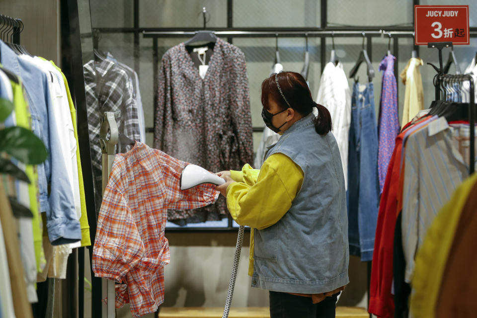 In this photo released by Xinhua News Agency, a worker wearing a protective face mask irons clothes at a re-opened shopping mall in in Wuhan in central China's Hubei province, Monday, March 30, 2020. Shopkeepers in the city at the center of China's virus outbreak were reopening Monday but customers were scarce after authorities lifted more of the anti-virus controls that kept tens of millions of people at home for two months. (Shen Bohan/Xinhua via AP)