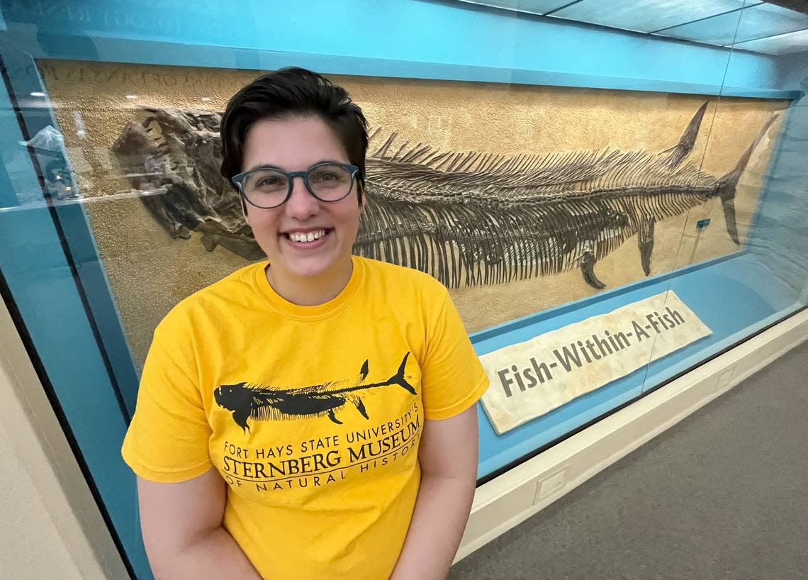 Aly Baumgartner stands in front of the Sternberg Museum’s famous fish-within-a-fish display, a fossil that’s also commemorated on her shirt.
