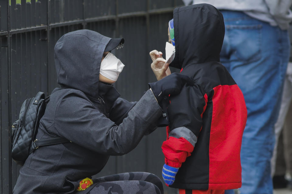 A woman adjusts her child's protective mask as they wait in line to be screened for COVID-19 at Gotham Health East New York, Thursday, April 23, 2020, in the Brooklyn borough of New York. (AP Photo/Frank Franklin II)